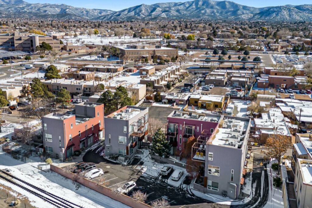 A cityscape with a mix of modern and older buildings, a railway track, and mountains in the background.