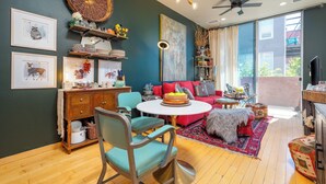 A cozy living room with a red sofa, teal chairs, a round coffee table, and a large painting on the wall. - Industrial Luxury Updated condo, 5 mins to Railyard, 7 mins to Plaza (Santa Fe)