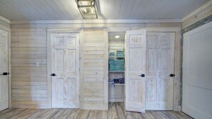 A room with wooden panel walls, a metal vent on the floor, and a closet with folded towels. - Colton's Cabin (Hawley)