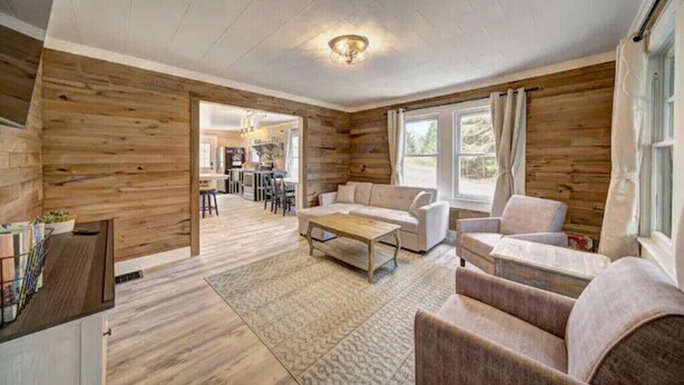 A spacious living area with wooden walls, a sofa, a coffee table, and a dining area visible through an open doorway. - Colton's Cabin (Hawley)