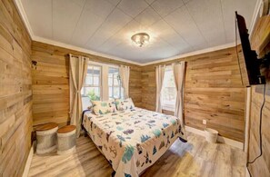 A wooden cabin bedroom with a bed, two windows, and a ceiling light.