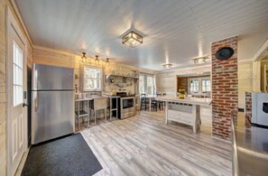 A spacious kitchen with wooden flooring, a stainless steel refrigerator, and a brick accent wall.
