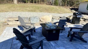 A patio with Adirondack chairs, a glass-top table, and a grill. - Colton's Cabin (Hawley)