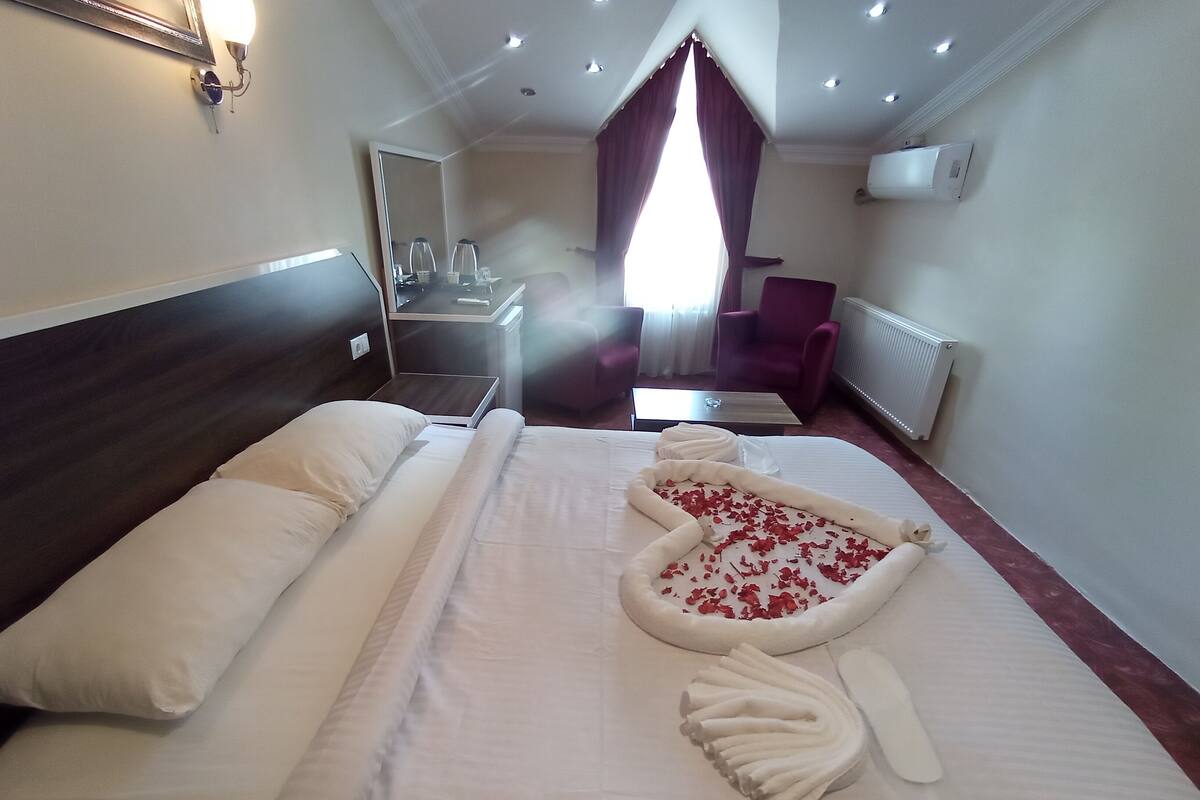 A hotel room with a bed, a mirror, a chair, a table, and a window with curtains.