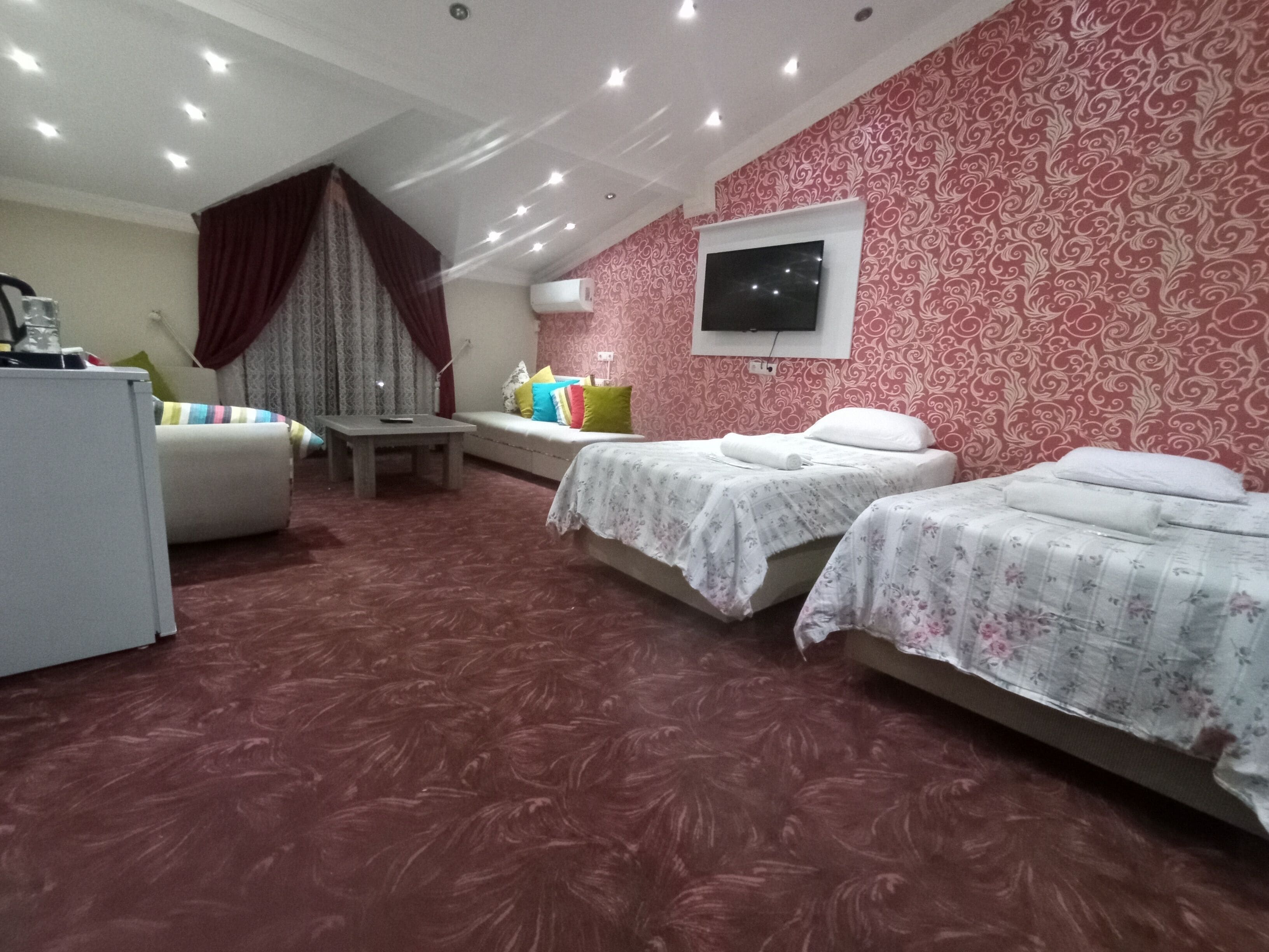 A hotel room with two beds, a sofa, a small table, and a TV mounted on the wall.