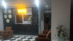 Un vestíbulo con suelo a cuadros, una zona de recepción con un letrero de neón y varios relojes en la pared.