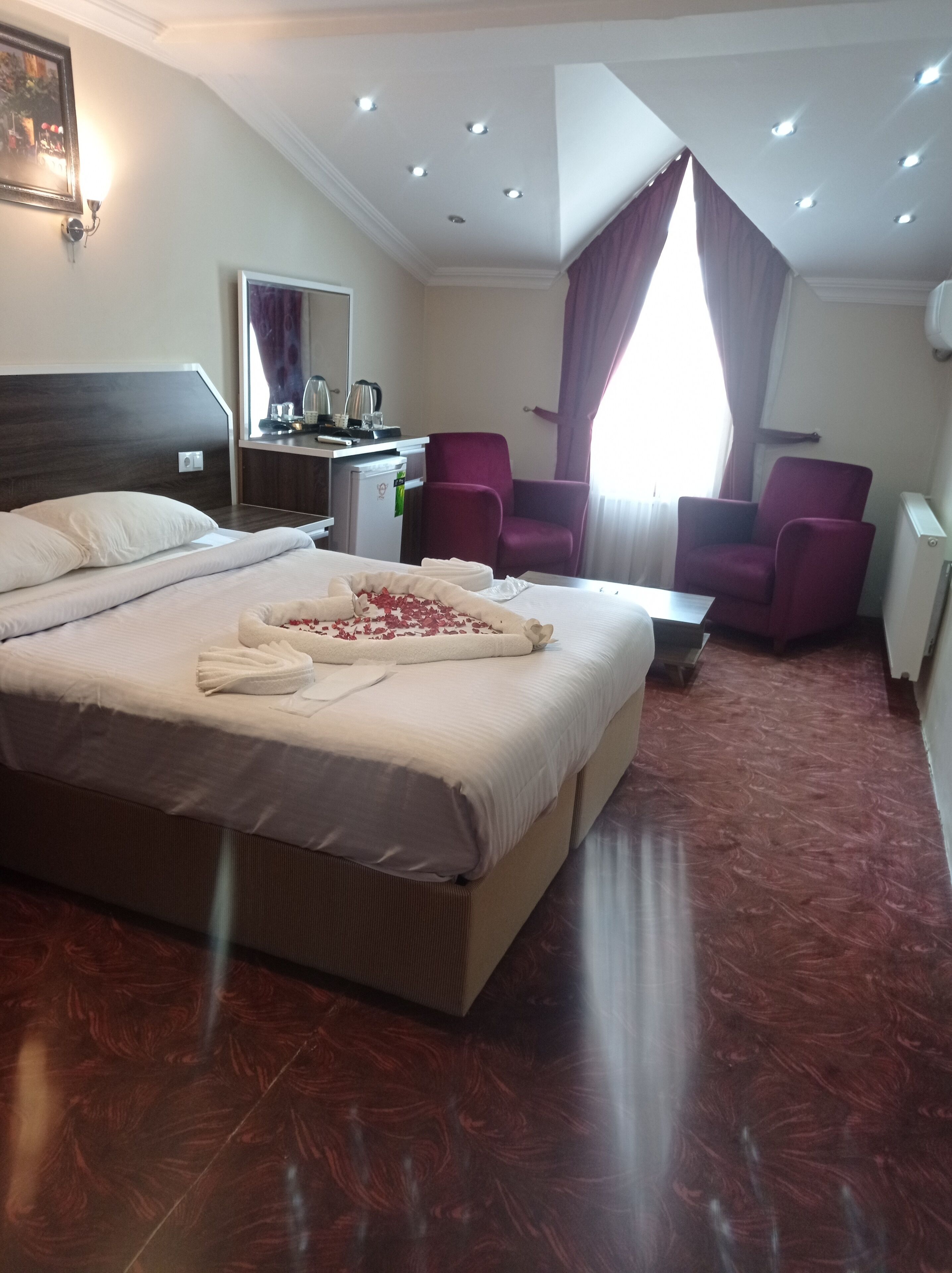 A hotel room with a large bed, two chairs, a small table, and a desk with a mirror and a kettle.