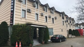Un hotel con un letrero que dice "CERENOTEL" y un número de teléfono. Se ven unidades de aire acondicionado en el edificio, un coche estacionado adelante y dos conos de tráfico cerca de la entrada.