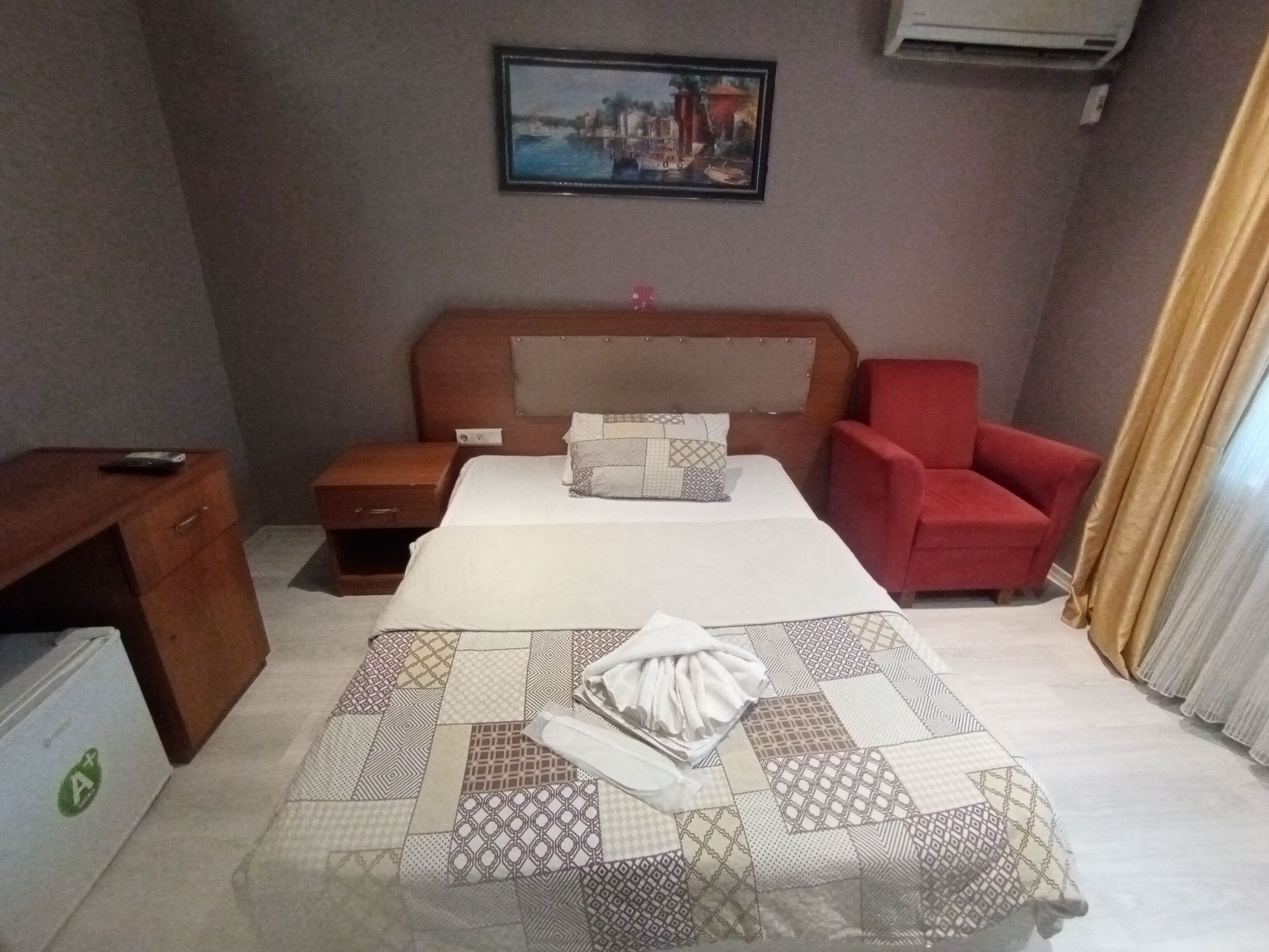 Habitación de hotel con una cama, una mesita de noche, una silla roja, un escritorio y un cuadro en la pared.