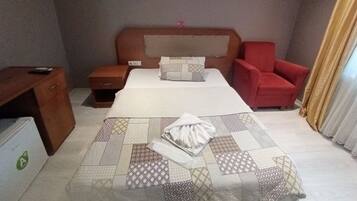 Habitación de hotel con una cama, una mesita de noche, una silla roja, un escritorio y un cuadro en la pared.