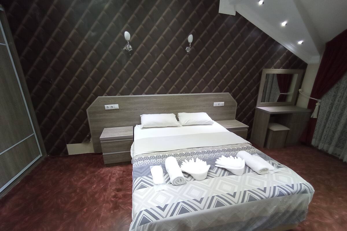 A hotel room with a bed, nightstand, mirror, and a small desk.
