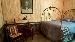 Une chambre avec une tête de lit en bois, un lit simple, une chaise avec un coussin et une petite table avec une lampe.