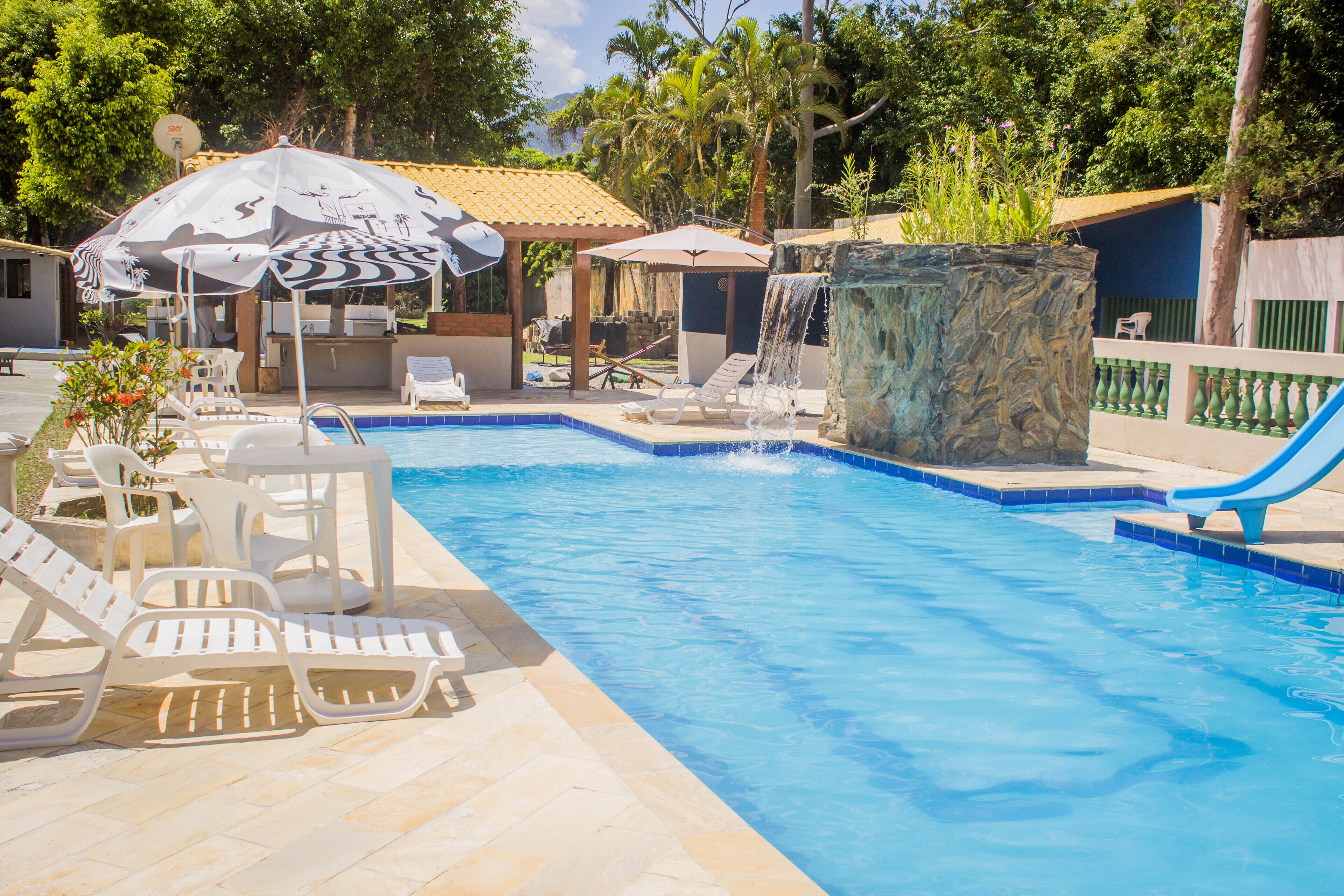 A swimming pool with lounge chairs and umbrellas, a water slide, and a waterfall feature.