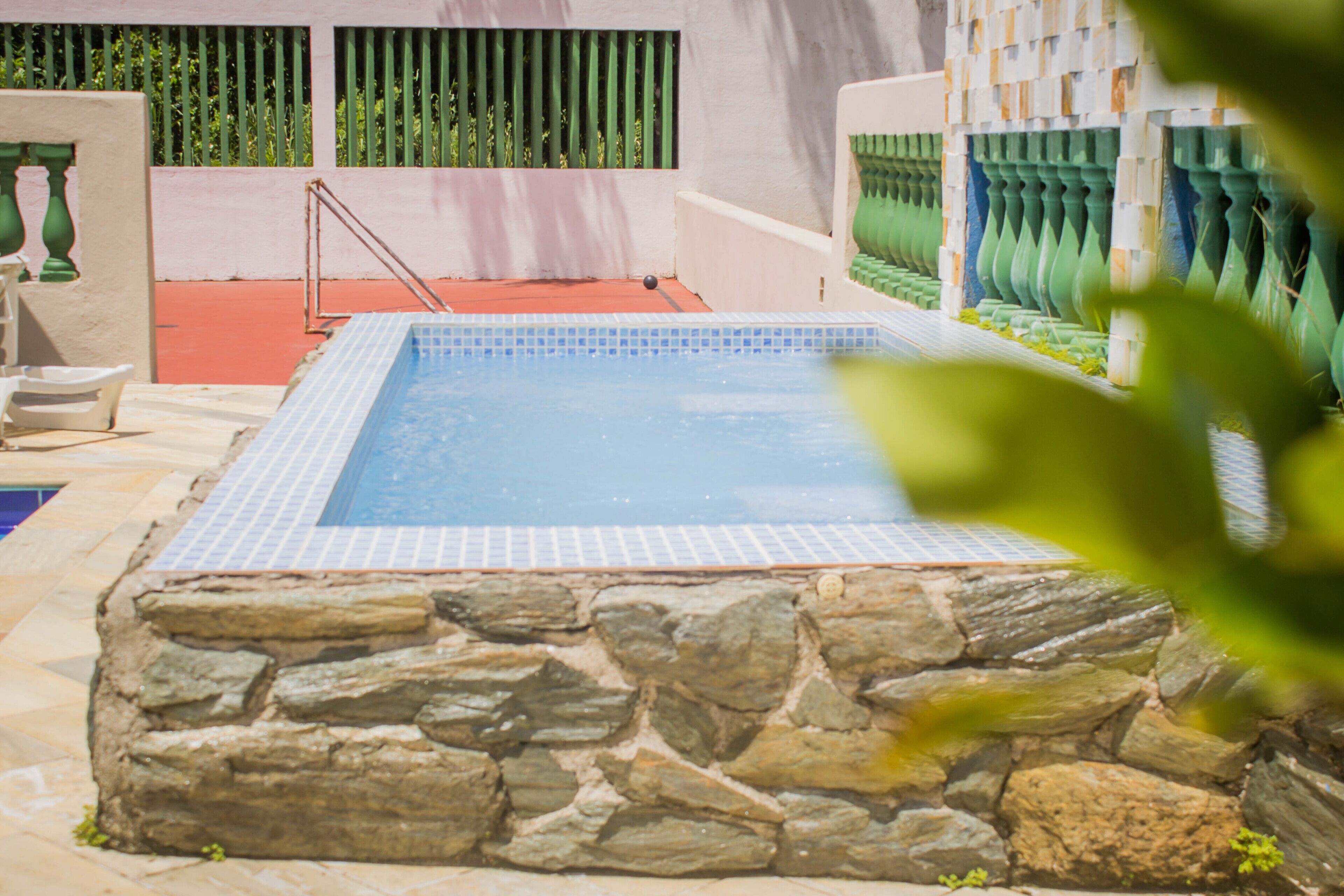 Una piscina con paredes de piedra y borde de azulejos, rodeada por un suelo rojo y barandillas verdes.