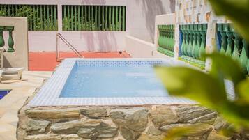 Una piscina con paredes de piedra y borde de azulejos, rodeada por un suelo rojo y barandillas verdes.