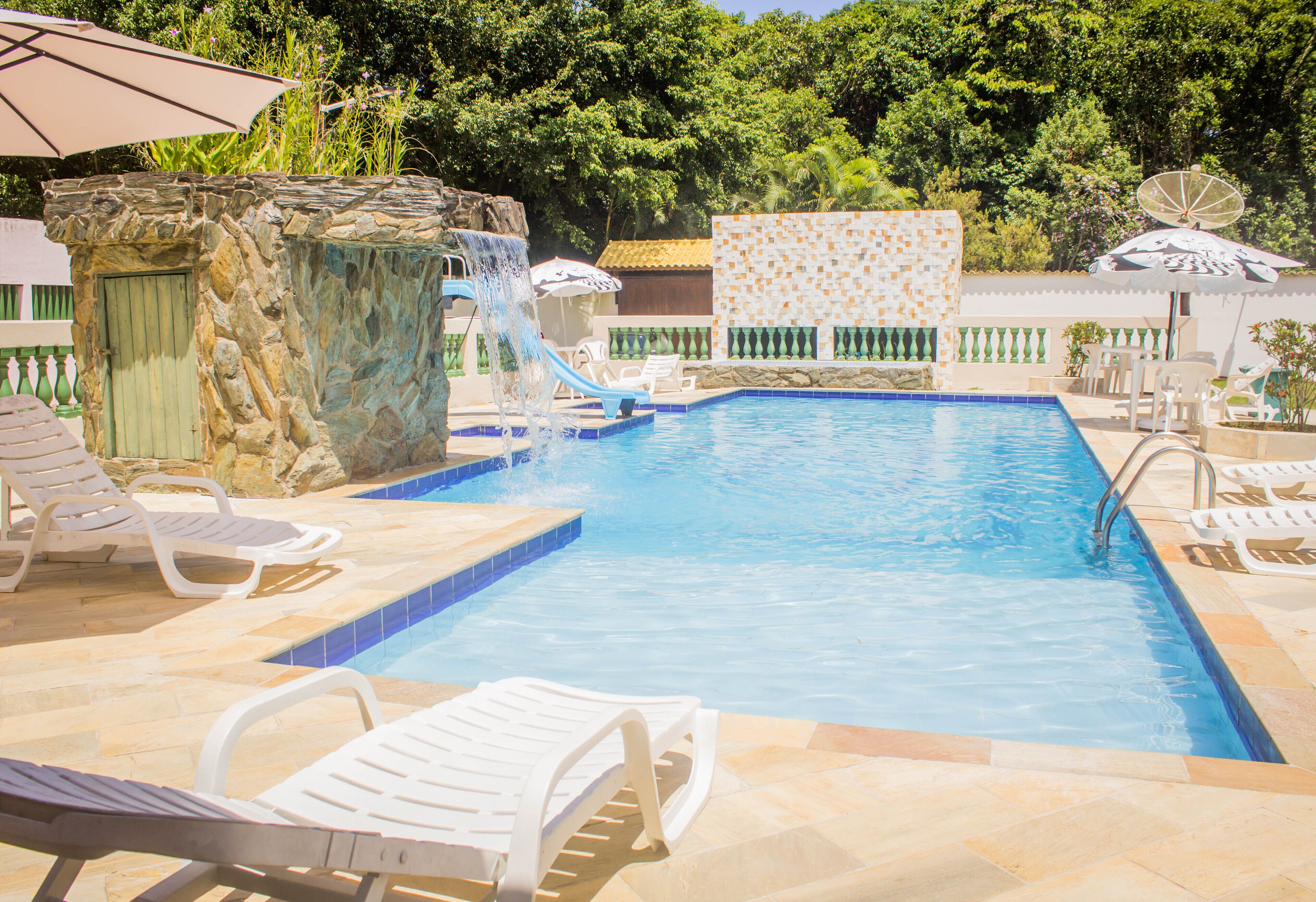 Une piscine agrémentée d’une cascade, entourée de chaises longues et de parasols.