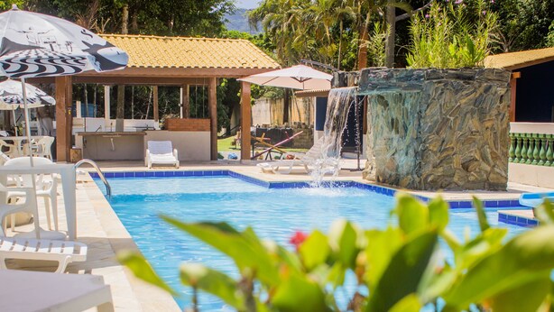 Une piscine dotée de chaises longues et de parasols, d’une cascade décorative et d’un jardinière en pierre.