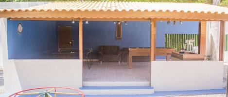 Uma área externa coberta com parede azul, uma mesa de madeira e uma cadeira.