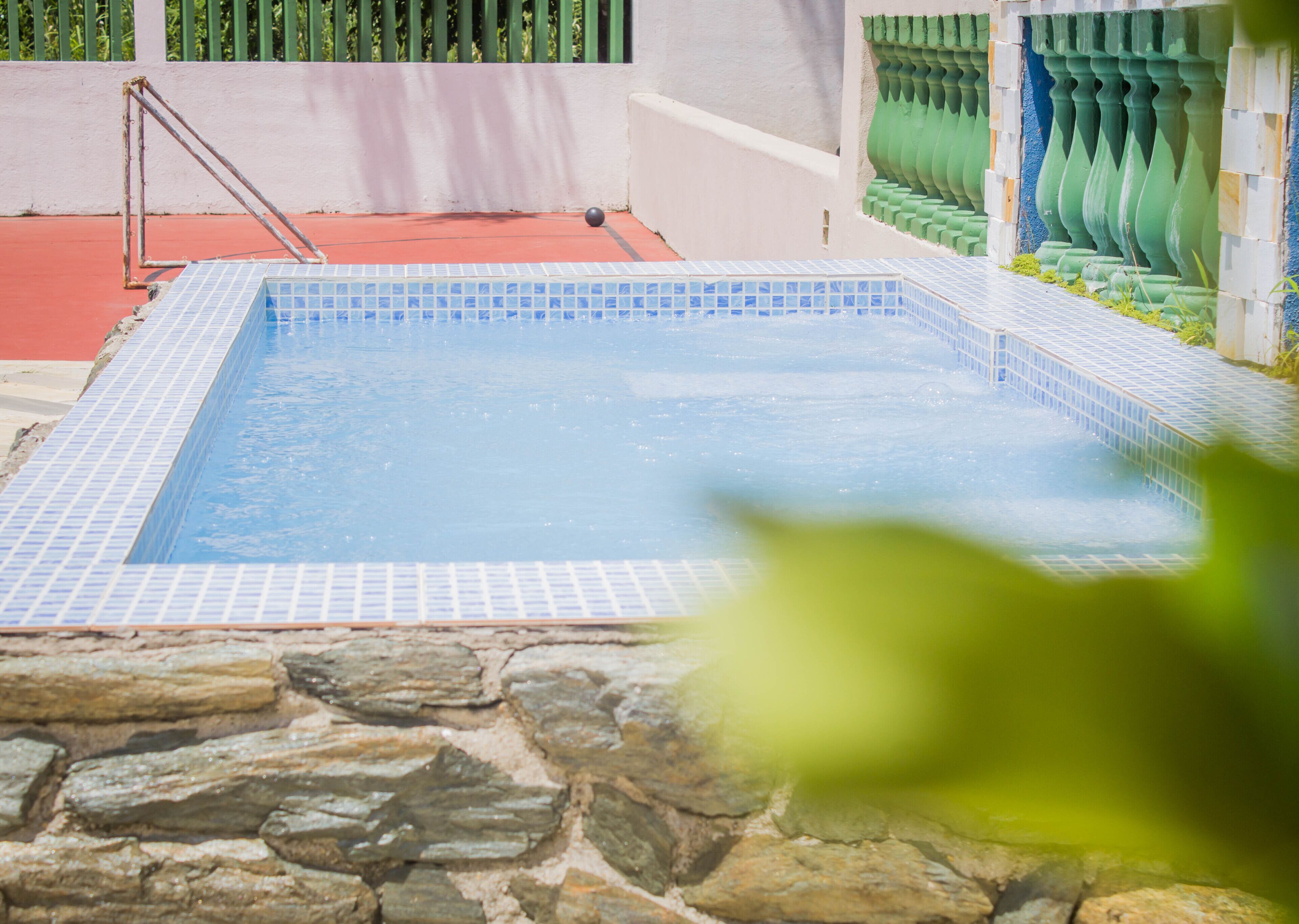 A swimming pool with a stone border, a metal ladder, and a red floor.