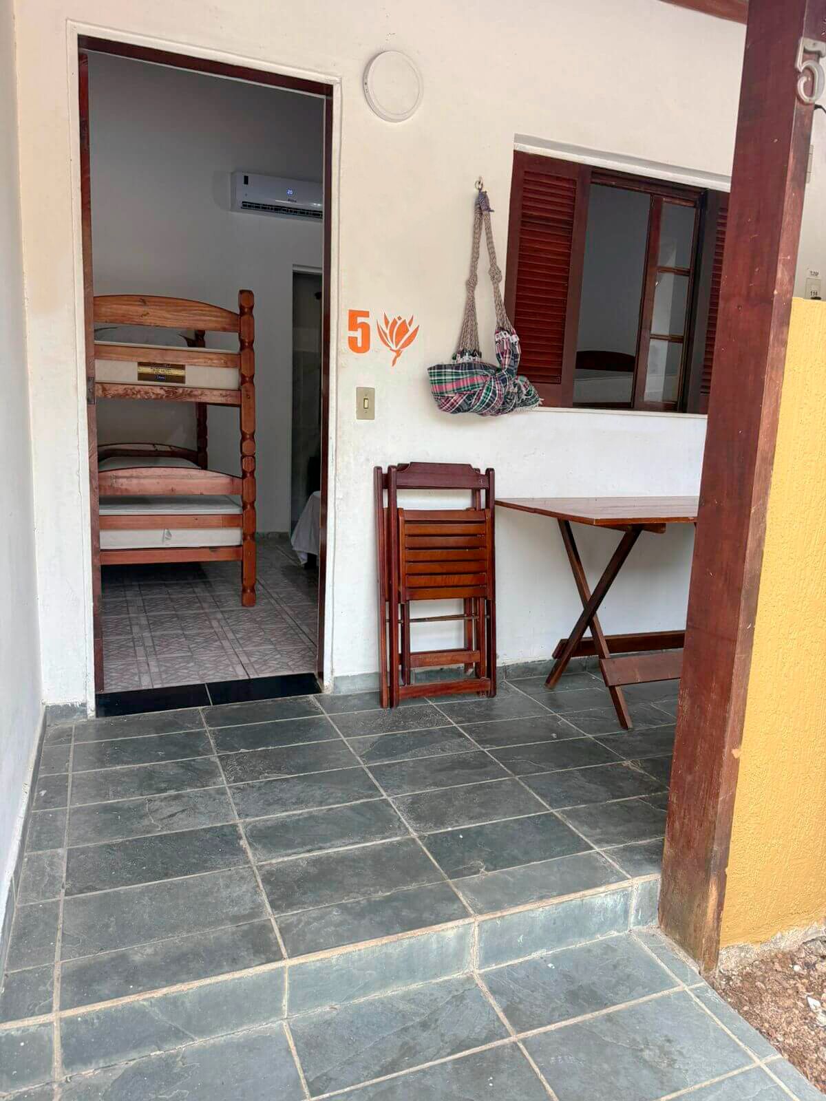 Une chambre avec un lit superposé, une petite table, une chaise et une fenêtre avec des volets.