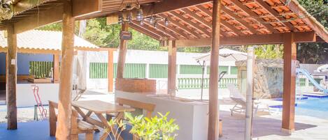 A covered patio area with a pool, wooden benches, and a table.