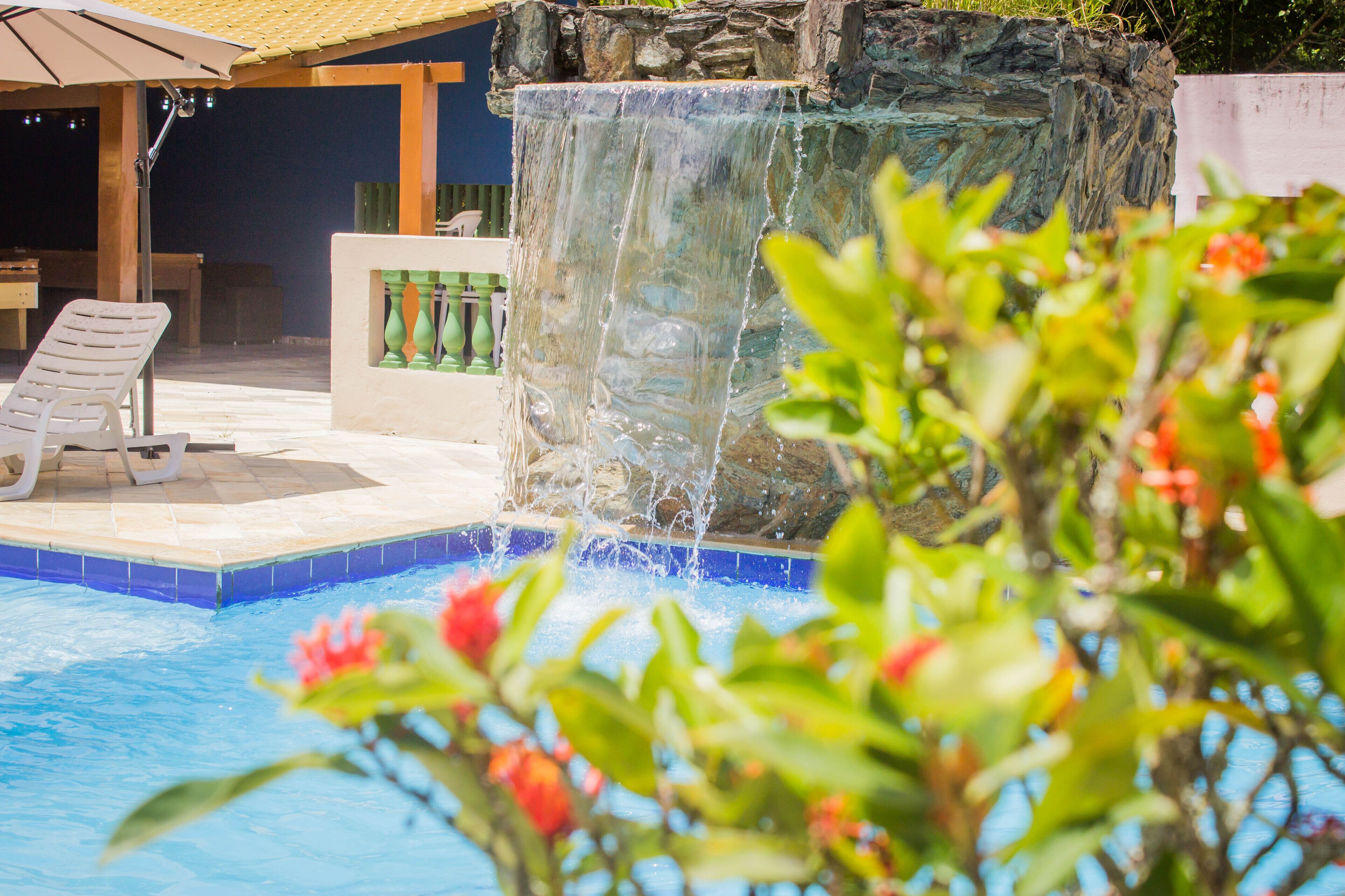Una piscina con una cascada, sillones de descanso y una zona de estar cubierta.