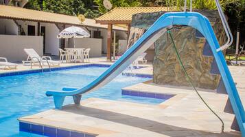 A swimming pool with a blue slide, lounge chairs, and a stone wall.