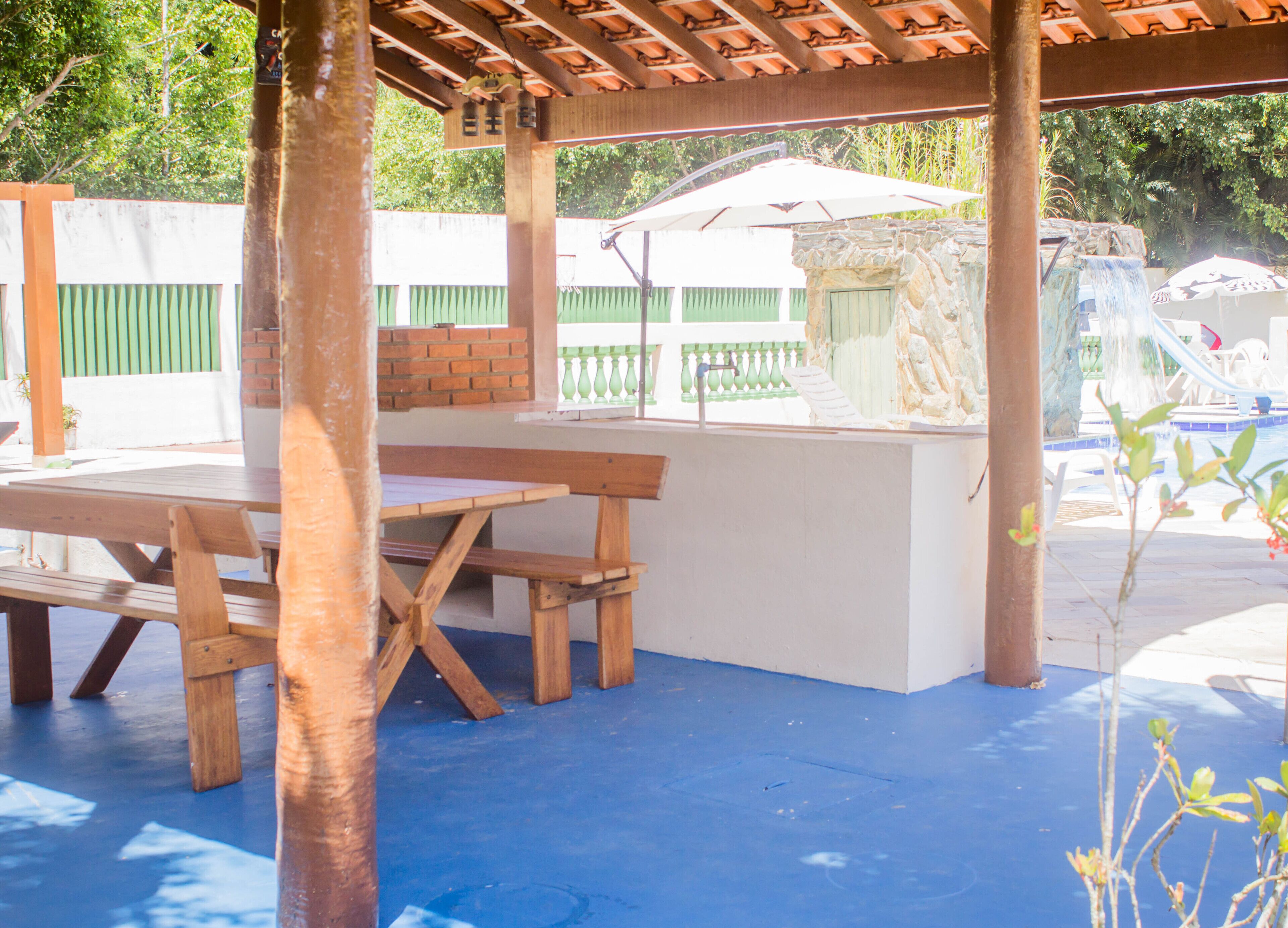 Un patio al aire libre con una mesa y bancos de madera, un muro de piedra y una piscina al fondo.