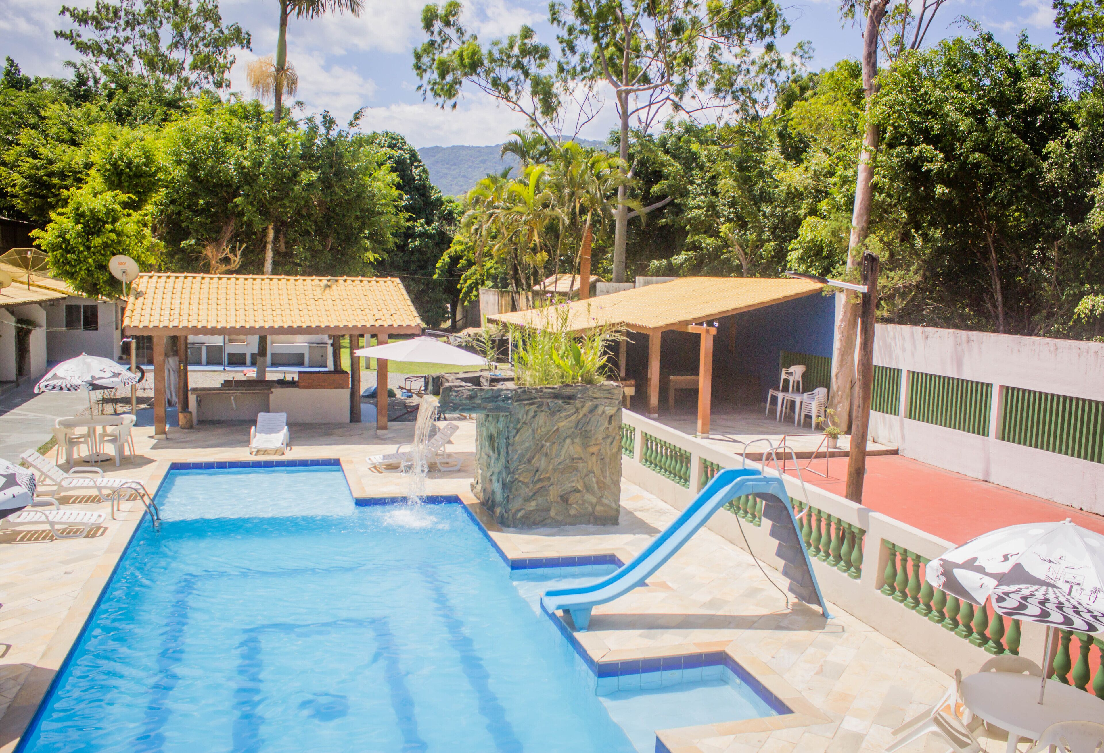 Una piscina con tobogán, sillas de descanso y sombrillas.