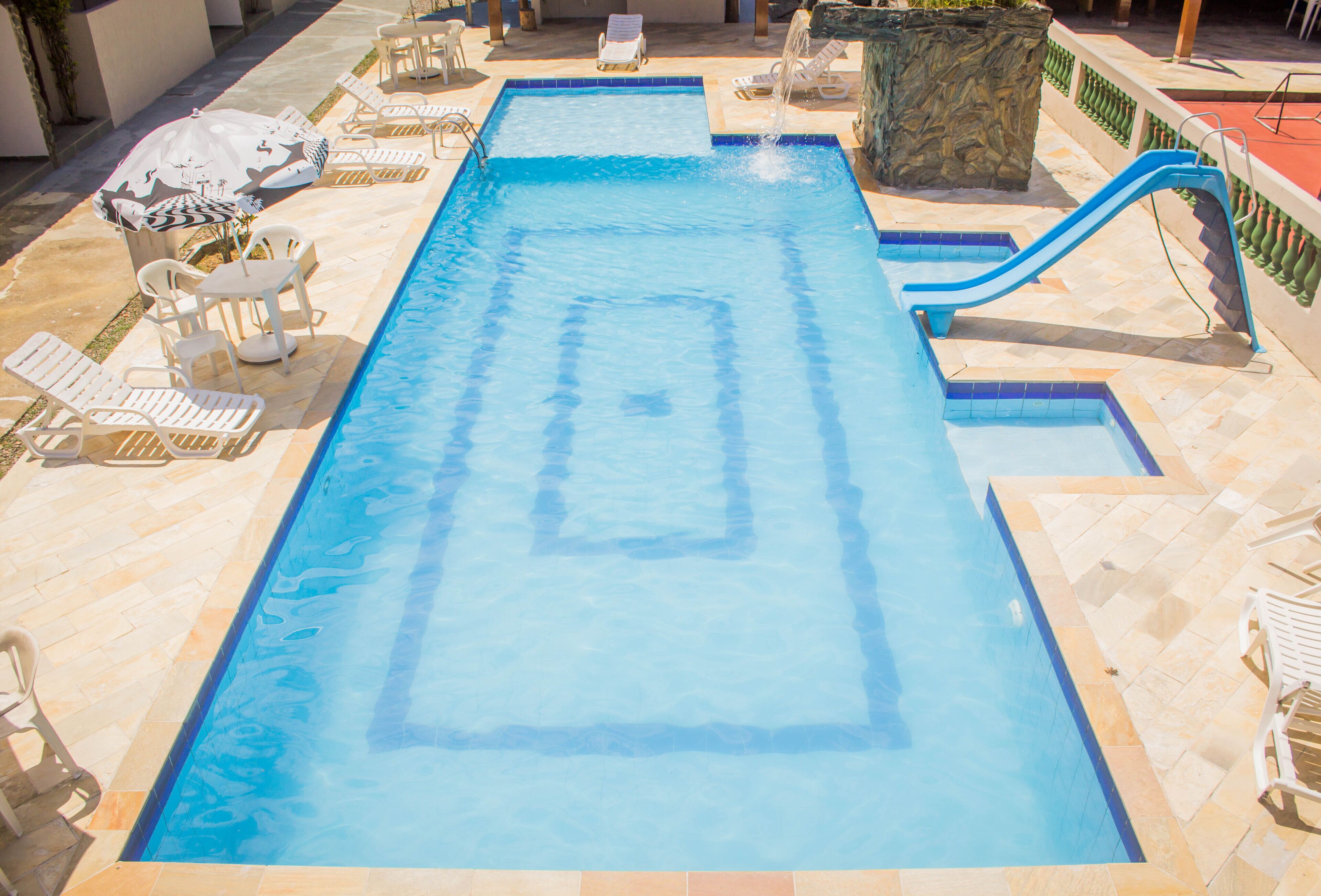 A rectangular swimming pool with a blue water feature, surrounded by white lounge chairs and a stone planter.