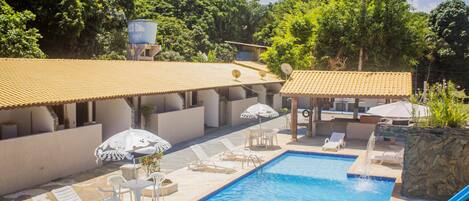 A pool area with lounge chairs and umbrellas, surrounded by buildings with tiled roofs.