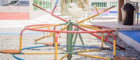 A playground with a multi-colored merry-go-round and a small pool area in the background.