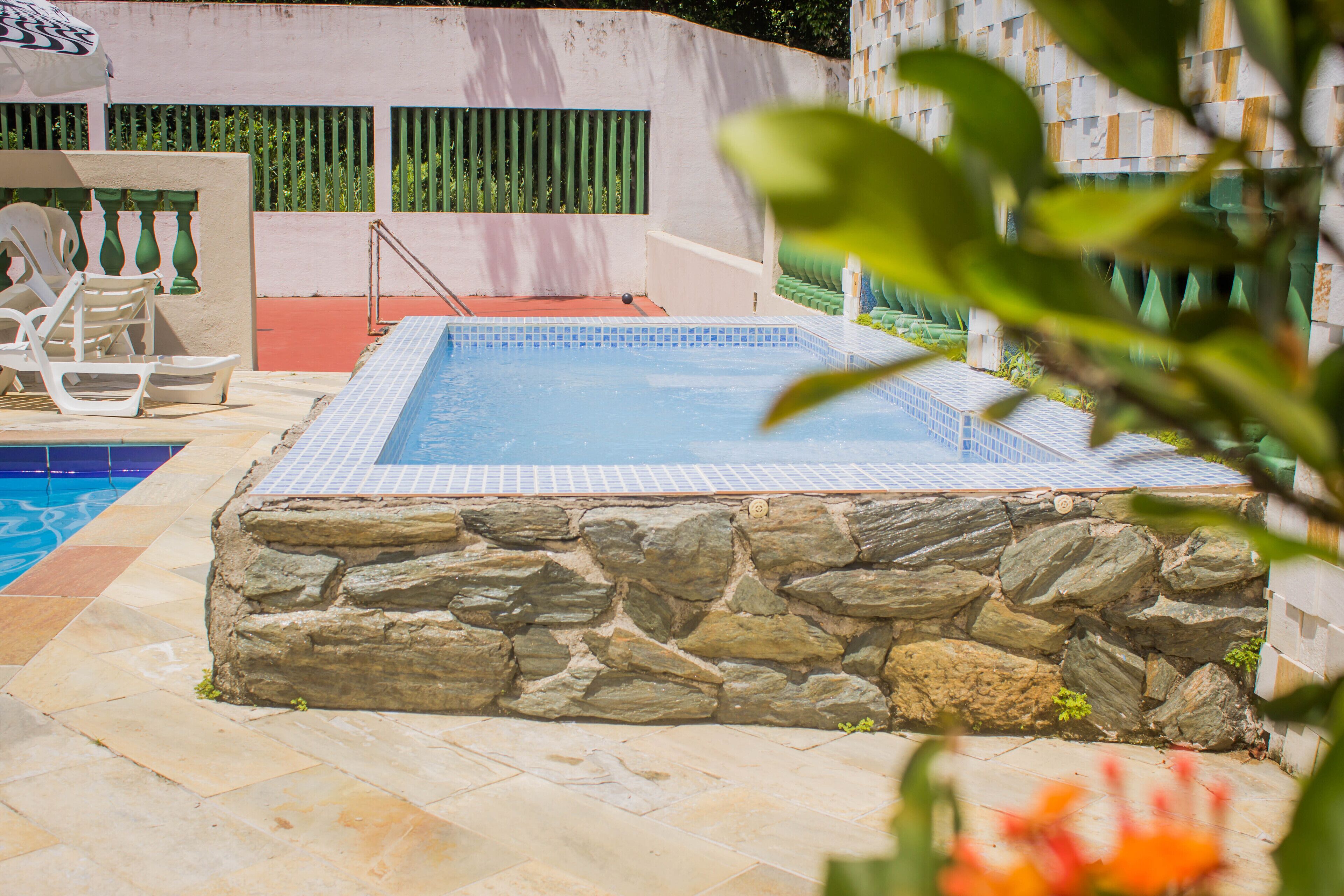 Una piscina circondata da muri in pietra, con un solarium piastrellato e lettini da relax.