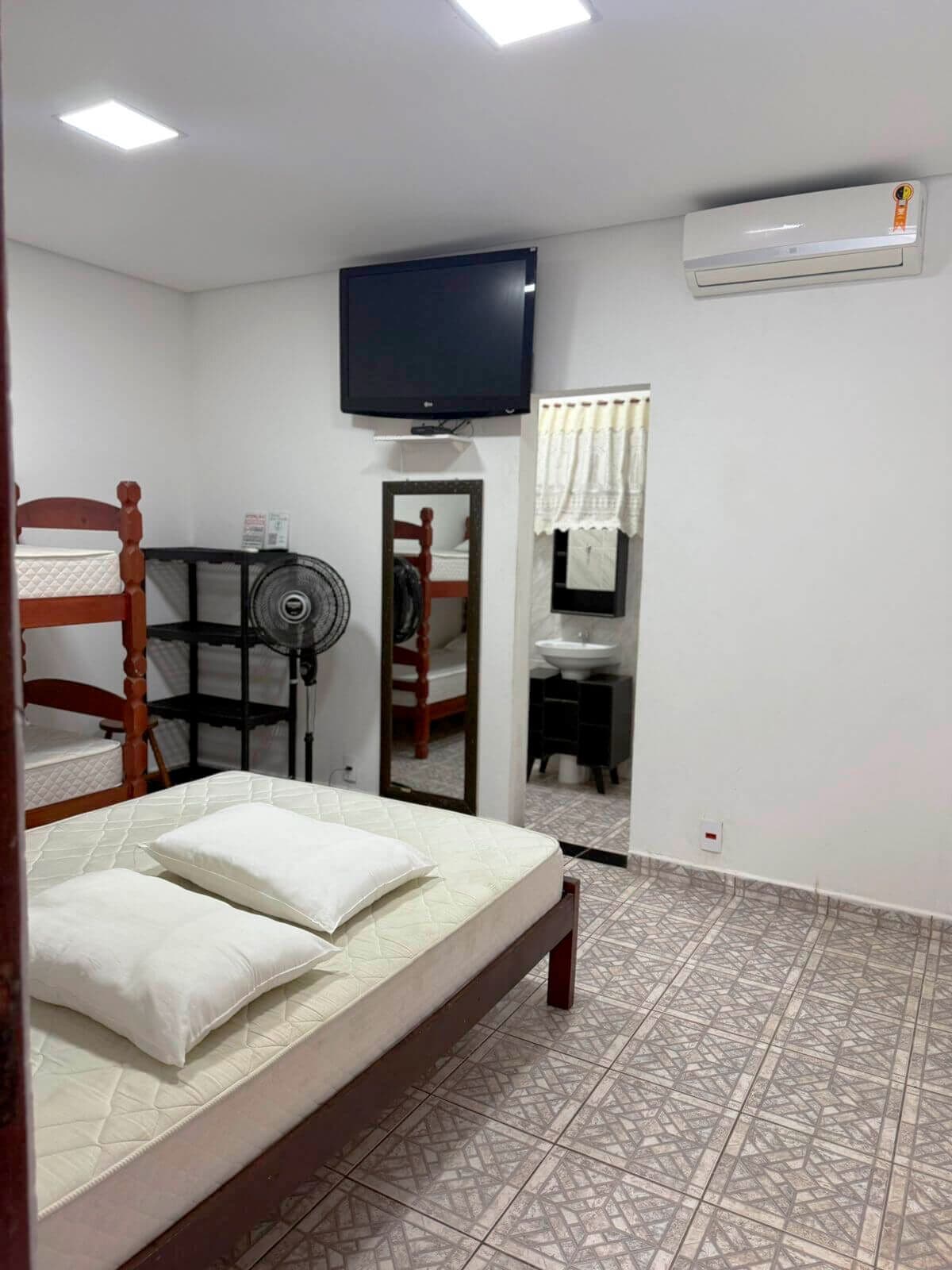 A bedroom with a bed, a TV, a fan, and a bathroom visible through an open door.