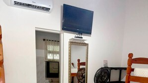 Une chambre d’hôtel avec un lit, un miroir, une télévision, un ventilateur et une chaise en bois.
