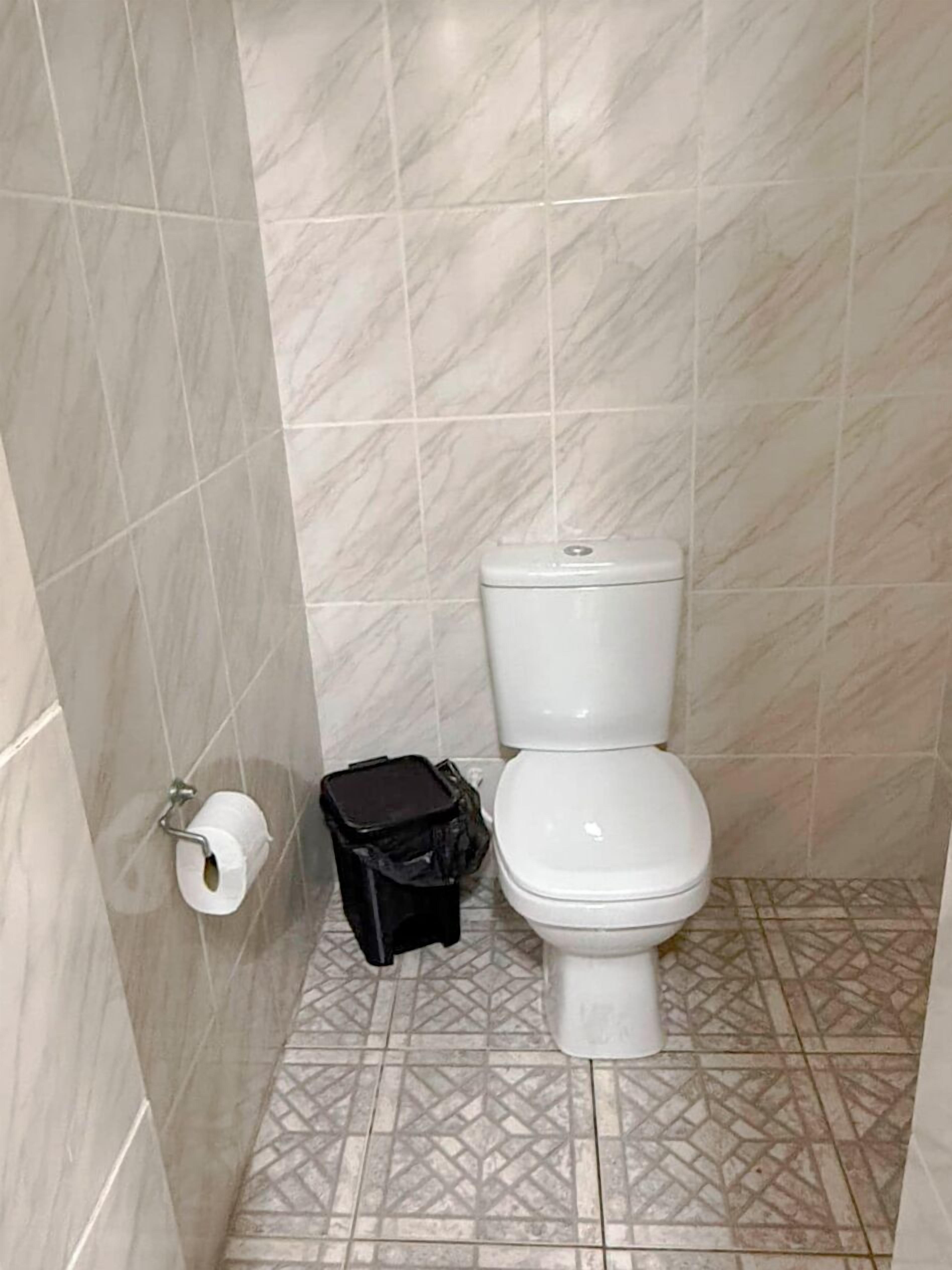 A small bathroom with a toilet, a trash bin, and a toilet paper holder on the wall.