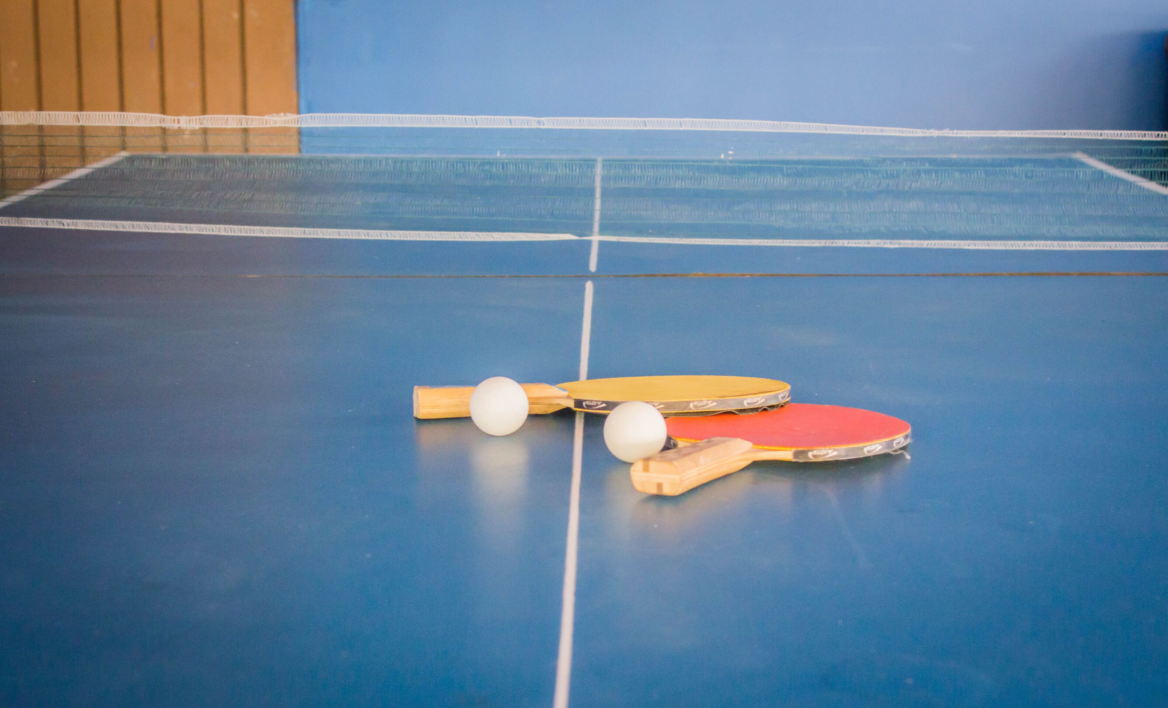 Una mesa de ping pong azul con dos palas y dos pelotas.