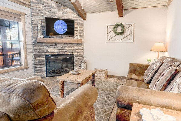 A cozy living room with a stone fireplace, a television mounted above it, and a comfortable sofa set. - Romantic Lakeview Cabin Near SDC with boat slip (Branson)