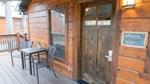 A wooden cabin with a porch, a table with chairs, and a welcome sign.