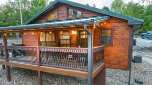 A wooden cabin with a covered porch, stone foundation, and a sign welcoming visitors.