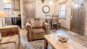 A cozy log cabin interior with a sofa, armchair, dining table, and wooden cabinets.