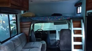 Interior de una caravana compacta con sofá, suelo de madera, una kitchenette pequeña y una ventana.