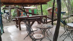 Un patio al aire libre con mesas y sillas de madera, un área de estar cubierta y vistas de la vegetación circundante.