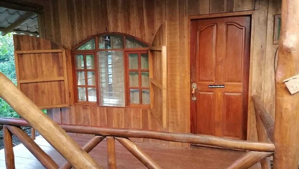 Una cabaña de madera con un ventanal grande, una puerta de madera y una barandilla de metal.