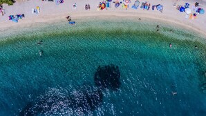 Vue aérienne d’une plage avec une eau turquoise cristalline, des parasols et des chaises de plage.