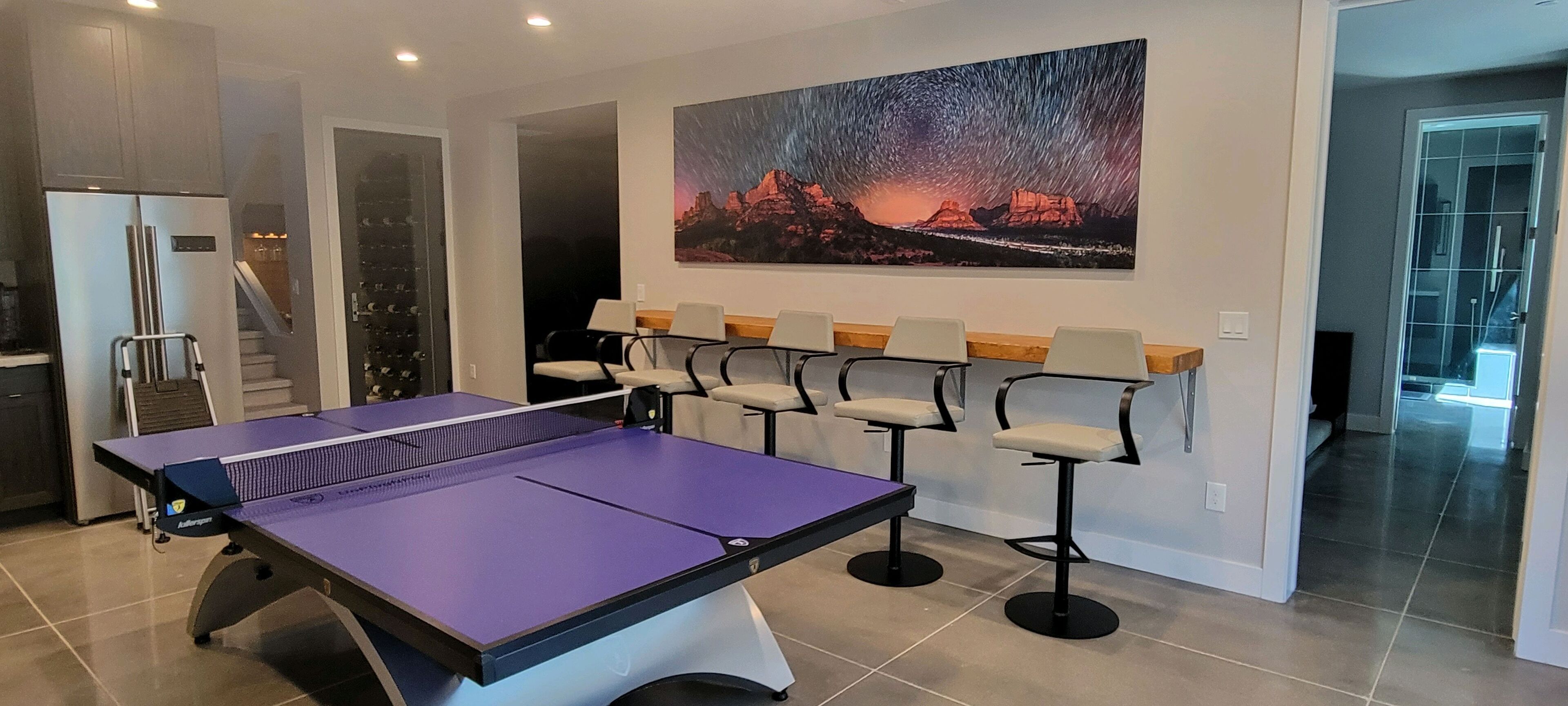 A ping pong table in a modern room with a staircase and a large painting of a night sky.