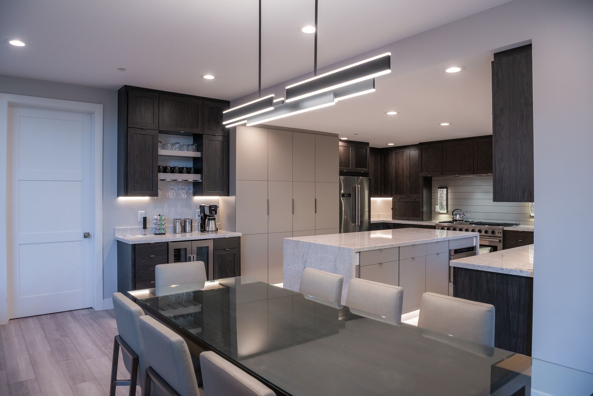 Una cocina moderna con armarios de madera oscura, una isla central y una zona de comedor con mesa y sillas de vidrio.