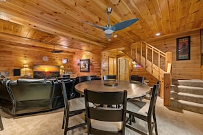 A cozy cabin interior with a round dining table, leather seating, a staircase, and wooden walls. - Copper Ridge Hideaway - Dog Friendly | Pac Man Arcade Game | Hot Tub (Mineral Bluff)