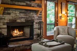 A cozy room with a stone fireplace, a comfortable armchair, and a view of greenery outside. - Copper Ridge Hideaway - Dog Friendly | Pac Man Arcade Game | Hot Tub (Mineral Bluff)