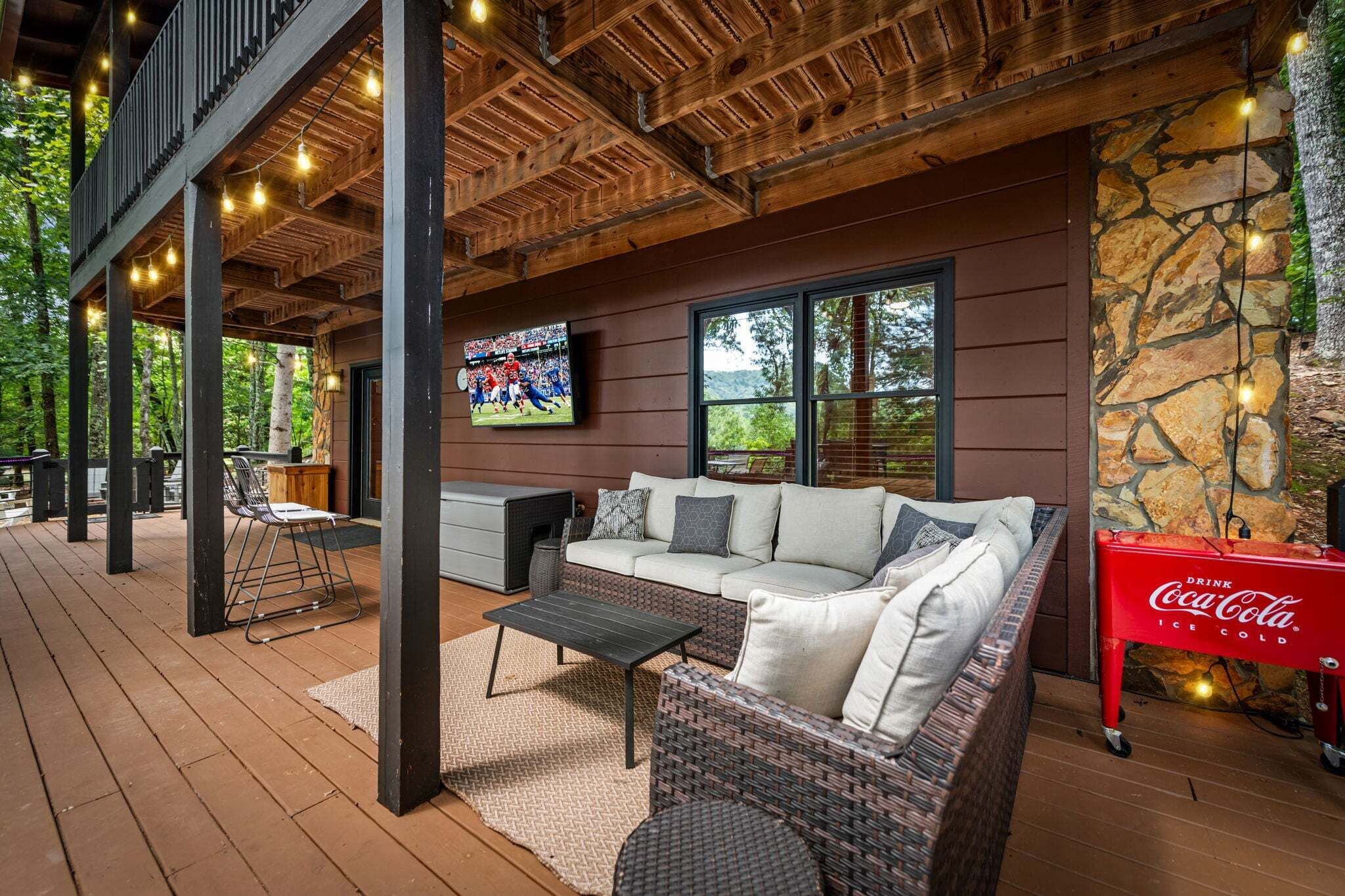 An outdoor seating area with a sofa, coffee table, and chairs, a stone wall, and a Coca-Cola cooler.